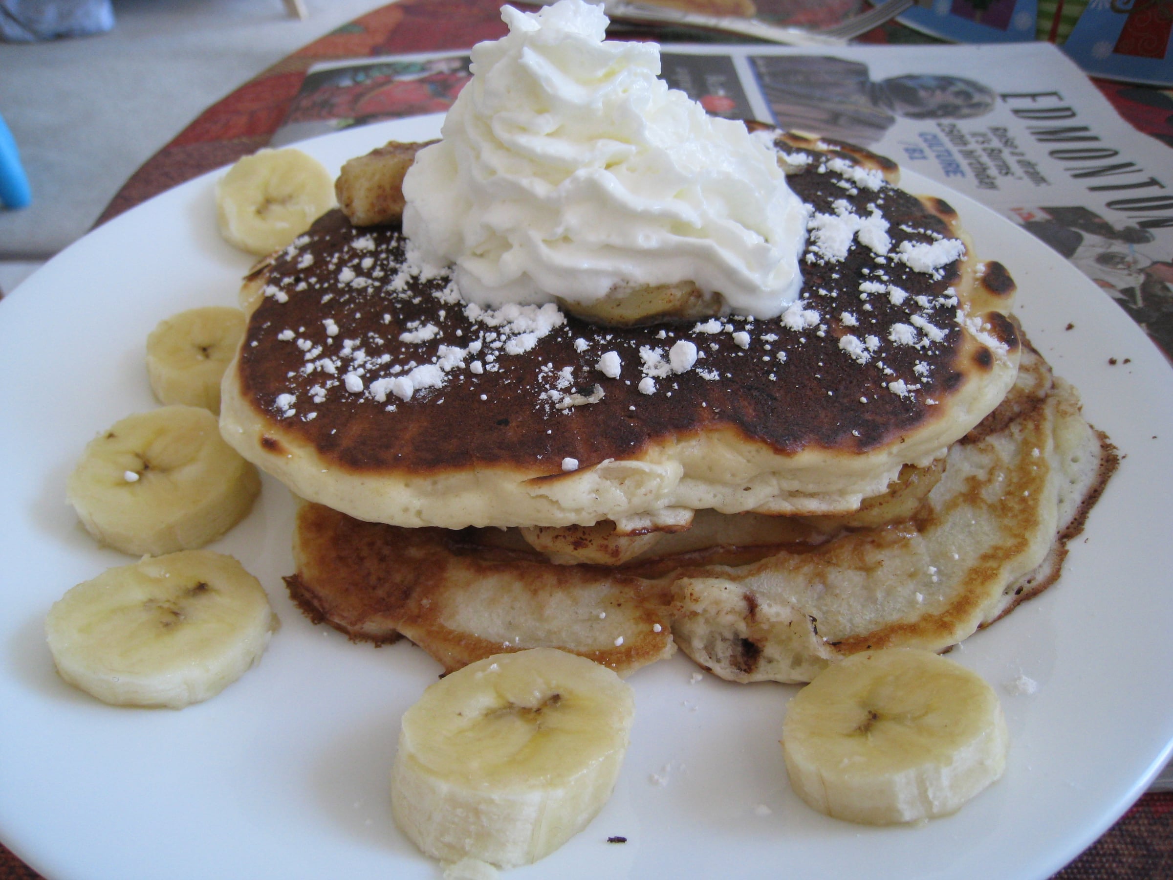 A stack of banana pancakes topped with cream and chocolate, with sliced banana around the plate
