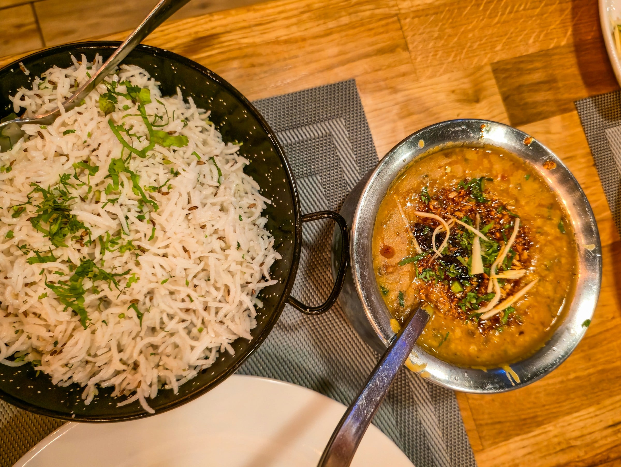 A bowl of golden lentil curry beside a pan of rice scattered with fresh coriander