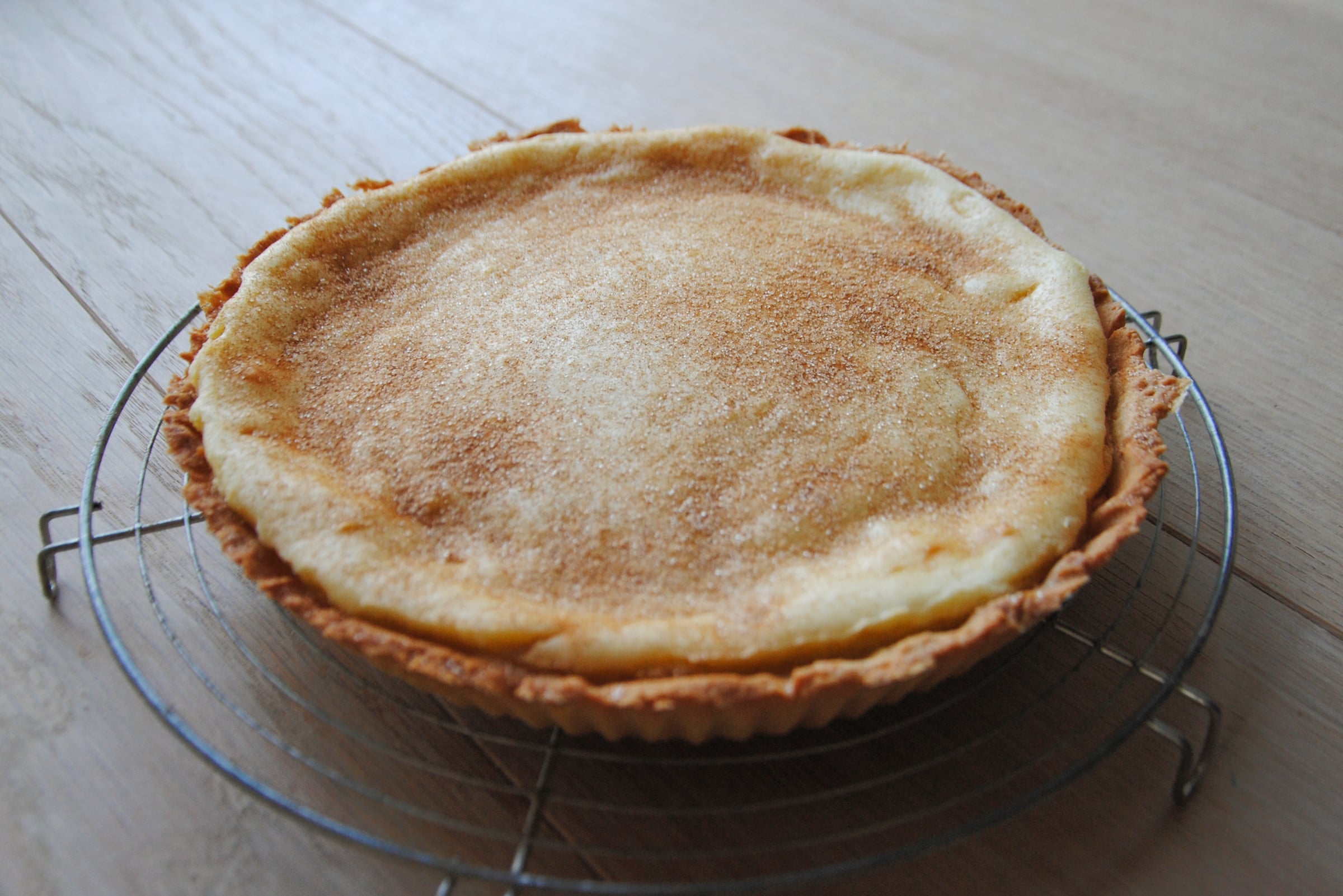 A whole melktert in its tin, the custard dusted with cinnamon, cooling on a rack
