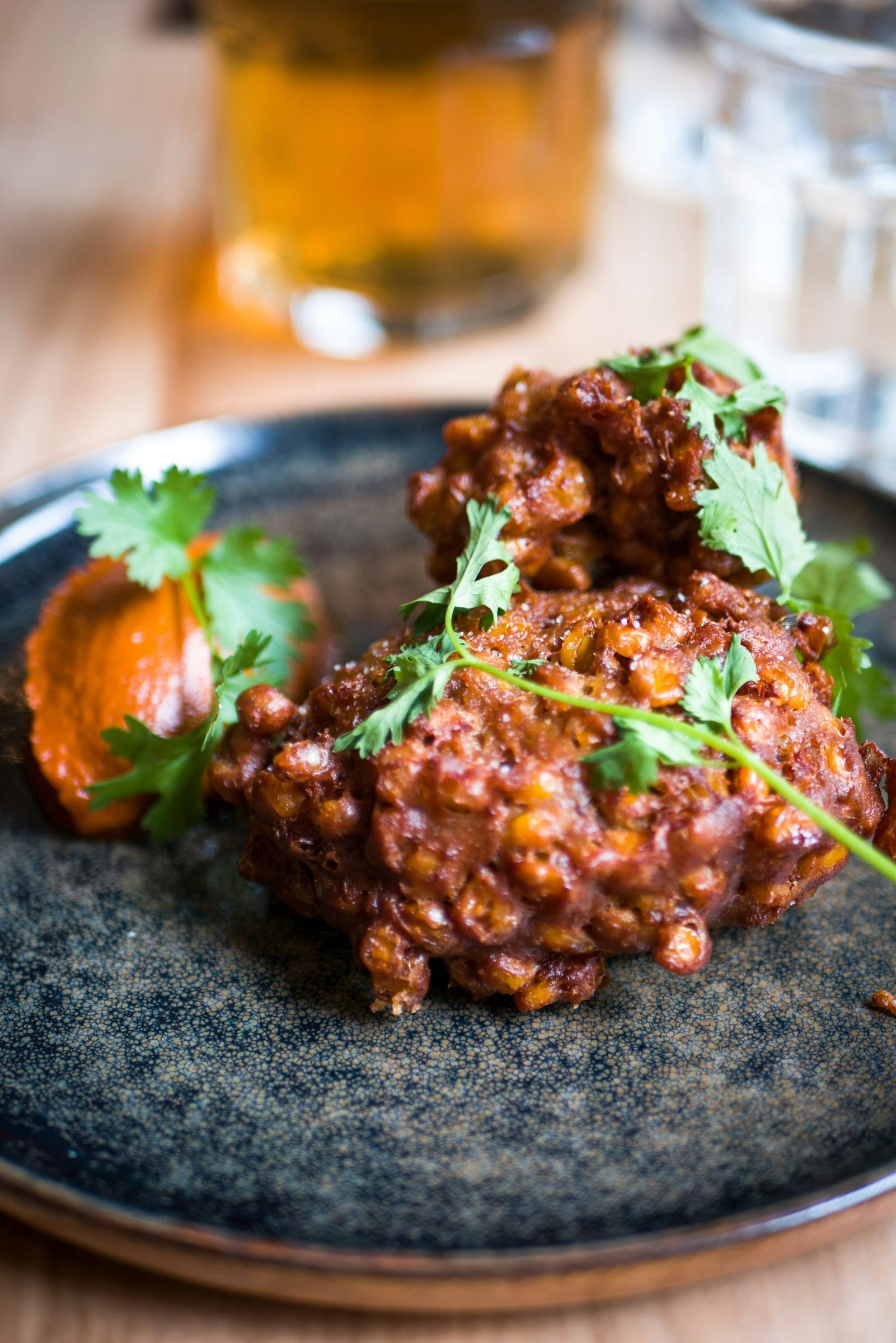 Crisp golden sweetcorn fritters on a dark plate, topped with fresh coriander