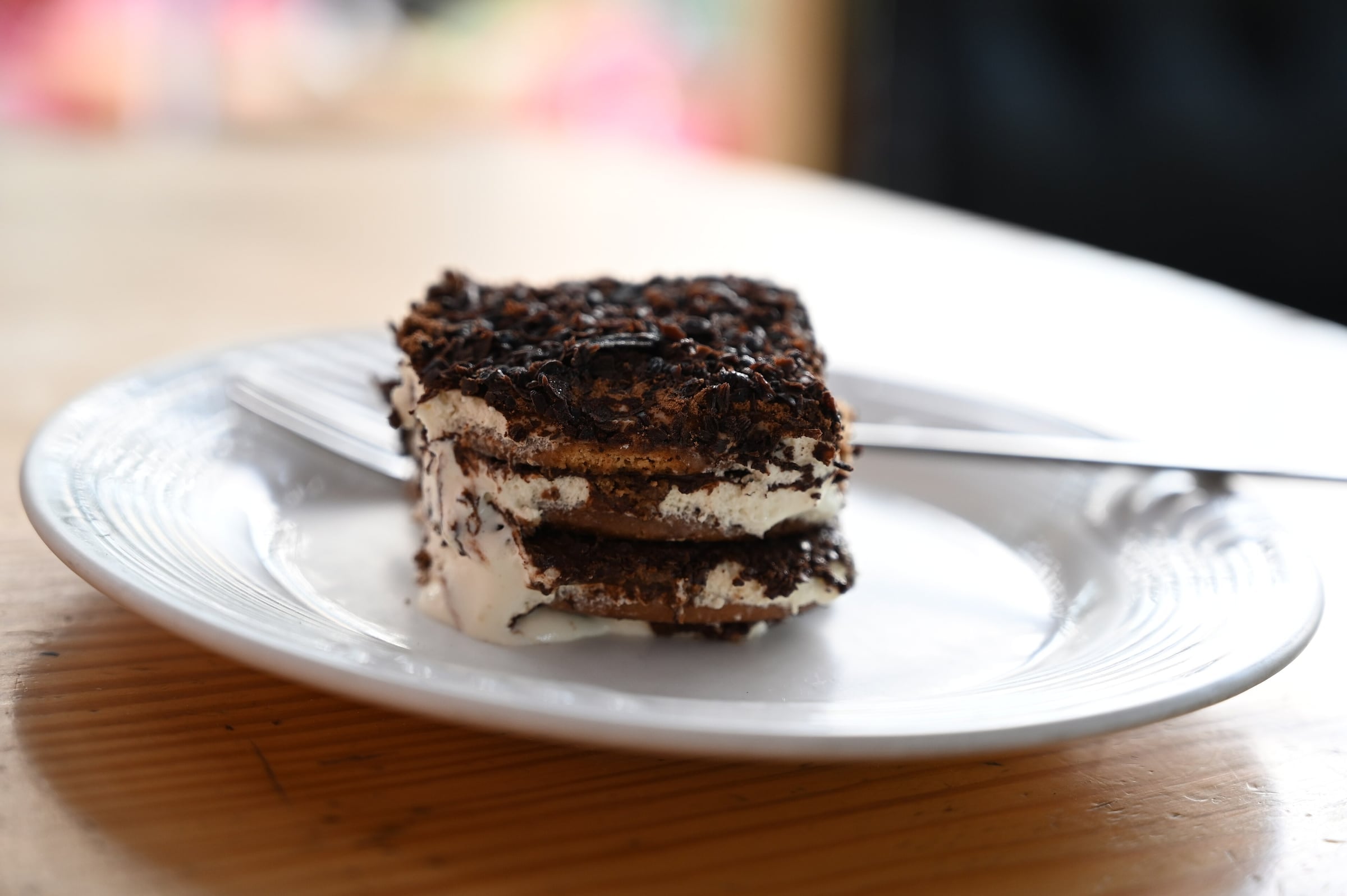 A slice of tiramisu on a plate showing layers of cream and coffee-soaked sponge under a cocoa dusting